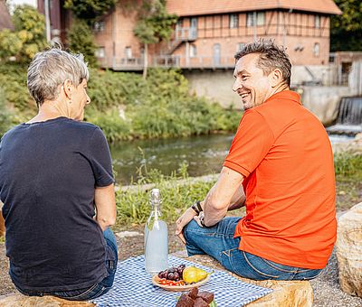 Zwei Personen machen eine Picknickpause an einem Fluss 